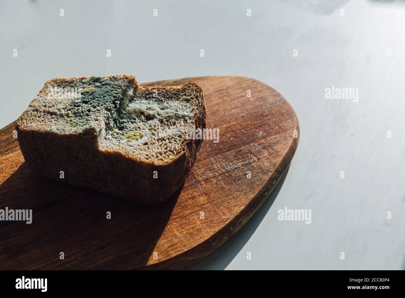 Molde sobre pan, un trozo de pan de centeno con molde blanco y verde sobre una tabla de madera. La fecha de mejor antes ha caducado. Foto de stock