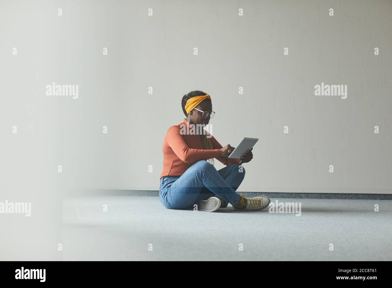 Mujer joven africana sentada en el suelo en una habitación vacía y usando una tableta digital ella trabaja en línea Foto de stock