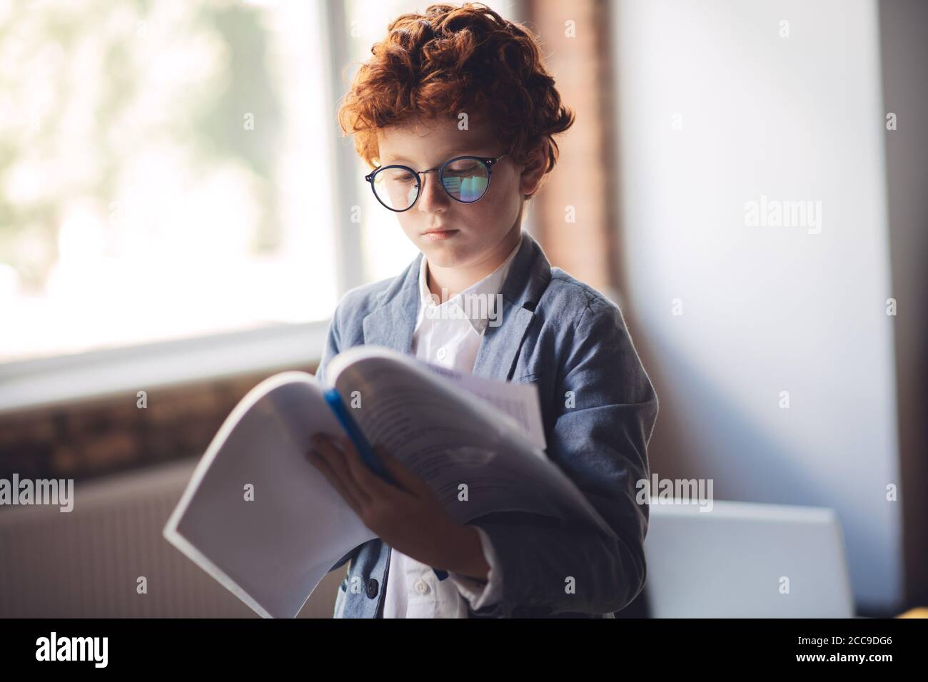 Niño de pelo rojo en un traje de leer un informe y mirar serio Foto de stock