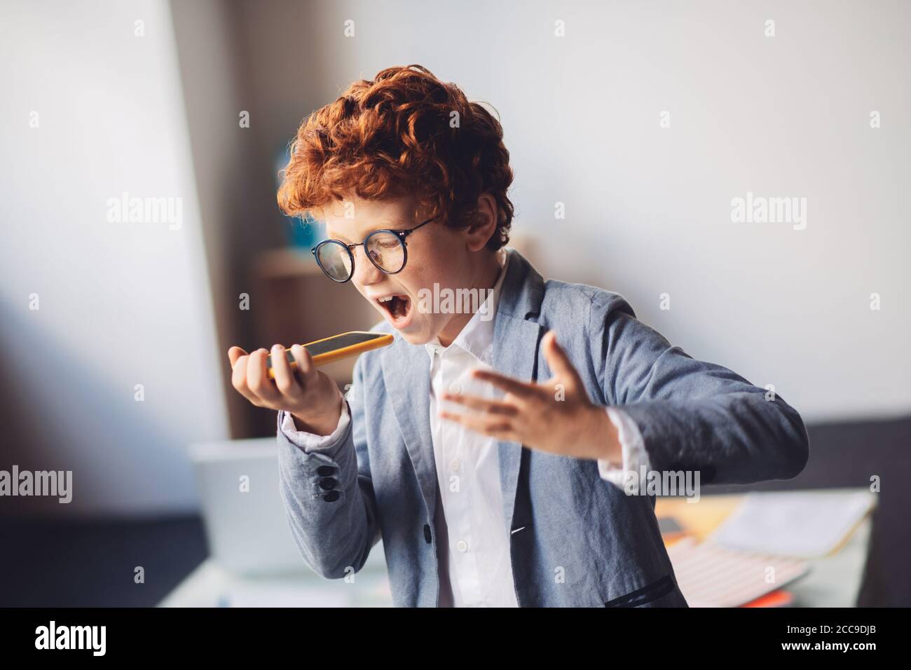 Niño de pelo rojo en un traje gritando algo mientras habla teléfono Foto de stock