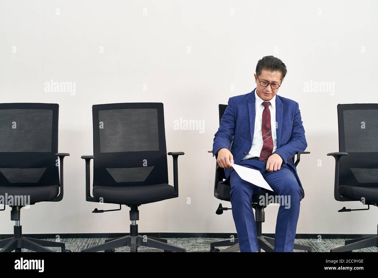un viejo buscador de trabajo asiático sentado en la silla parece ser frustrado y derrotado Foto de stock