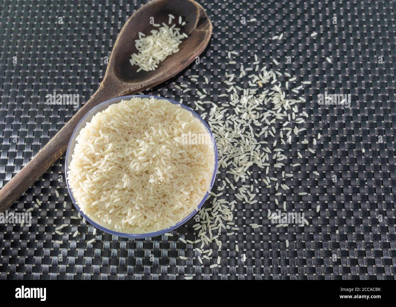 Arroz pelado y procesado de grano sobre fondo oscuro. Cereales de arroz y ornamentos de cocina. Granos semi-procesados en una olla de plástico y cucharas de madera. Foo Foto de stock