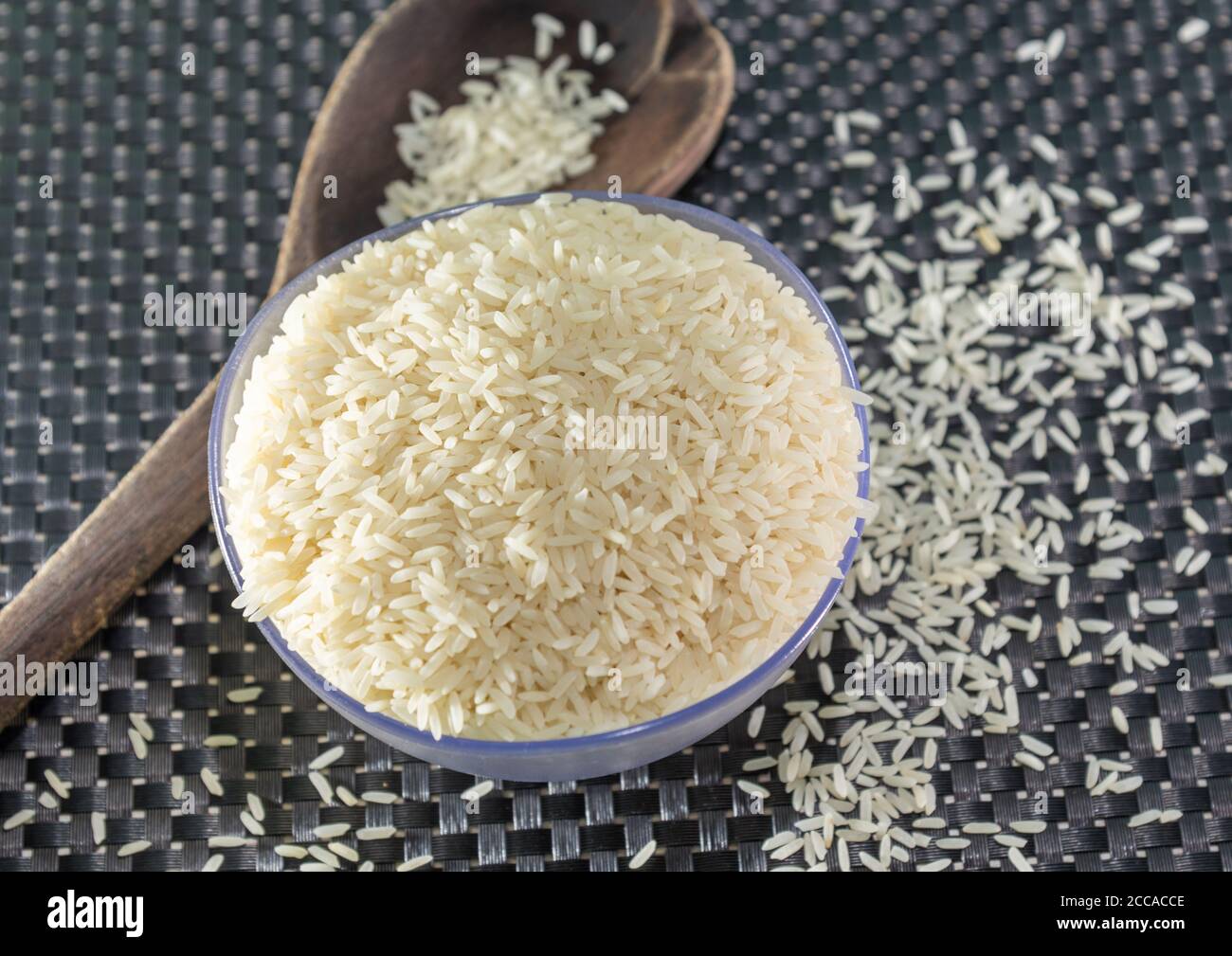 Arroz pelado y procesado de grano sobre fondo oscuro. Cereales de arroz y ornamentos de cocina. Granos semi-procesados en una olla de plástico y cucharas de madera. Foo Foto de stock