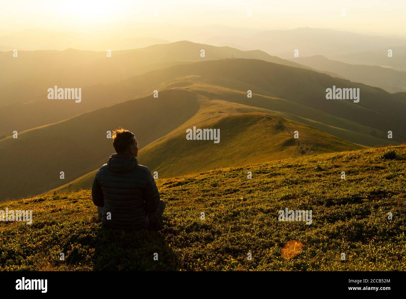 Solo turista en el borde de la colina de montaña contra el telón de fondo de un increíble paisaje de montañas al atardecer Foto de stock