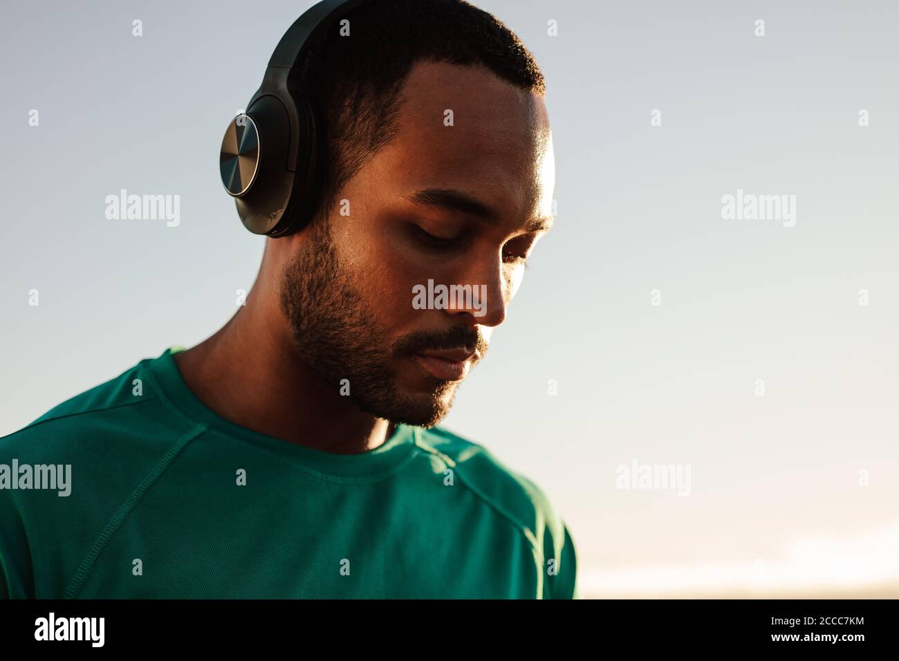 Retrato de un atleta afroamericano con auriculares inalámbricos. Primer plano de un hombre de fitness de pie al aire libre escuchando música. Foto de stock