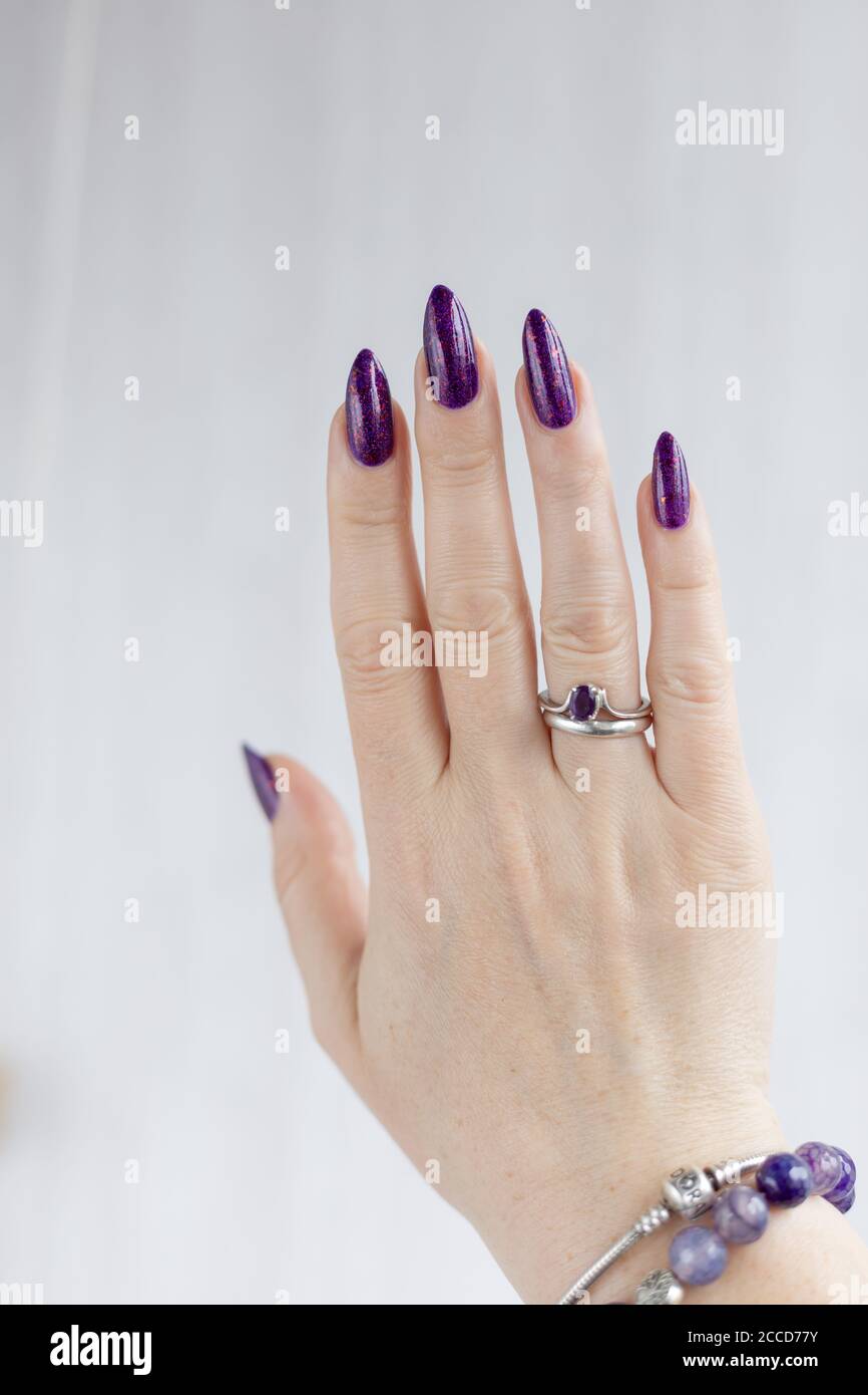 Mano femenina con uñas largas y manicura lila púrpura contiene una botella  de esmalte de uñas Fotografía de stock - Alamy