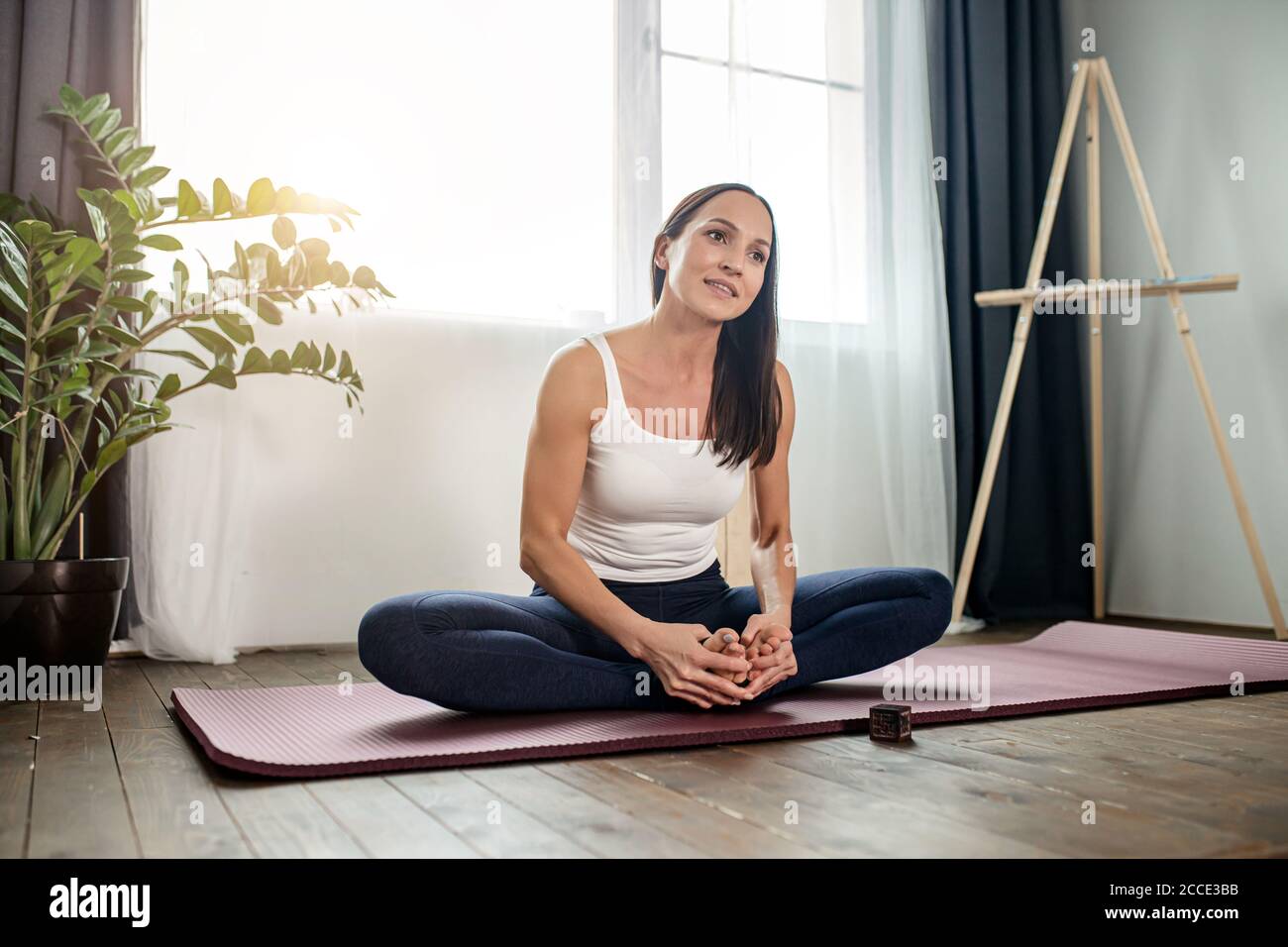 mujer relajada descansar después de los ejercicios de yoga, sentarse en el suelo con piernas cruzadas, en ropa deportiva en casa Foto de stock