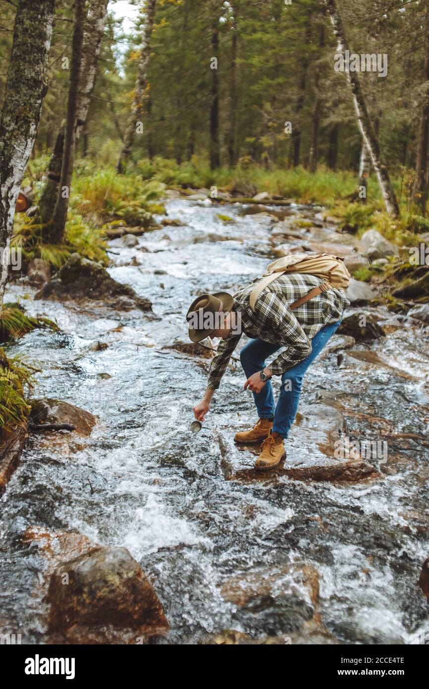 el joven hiker atrae agua fría en su taza, vista lateral completa photo.break Foto de stock