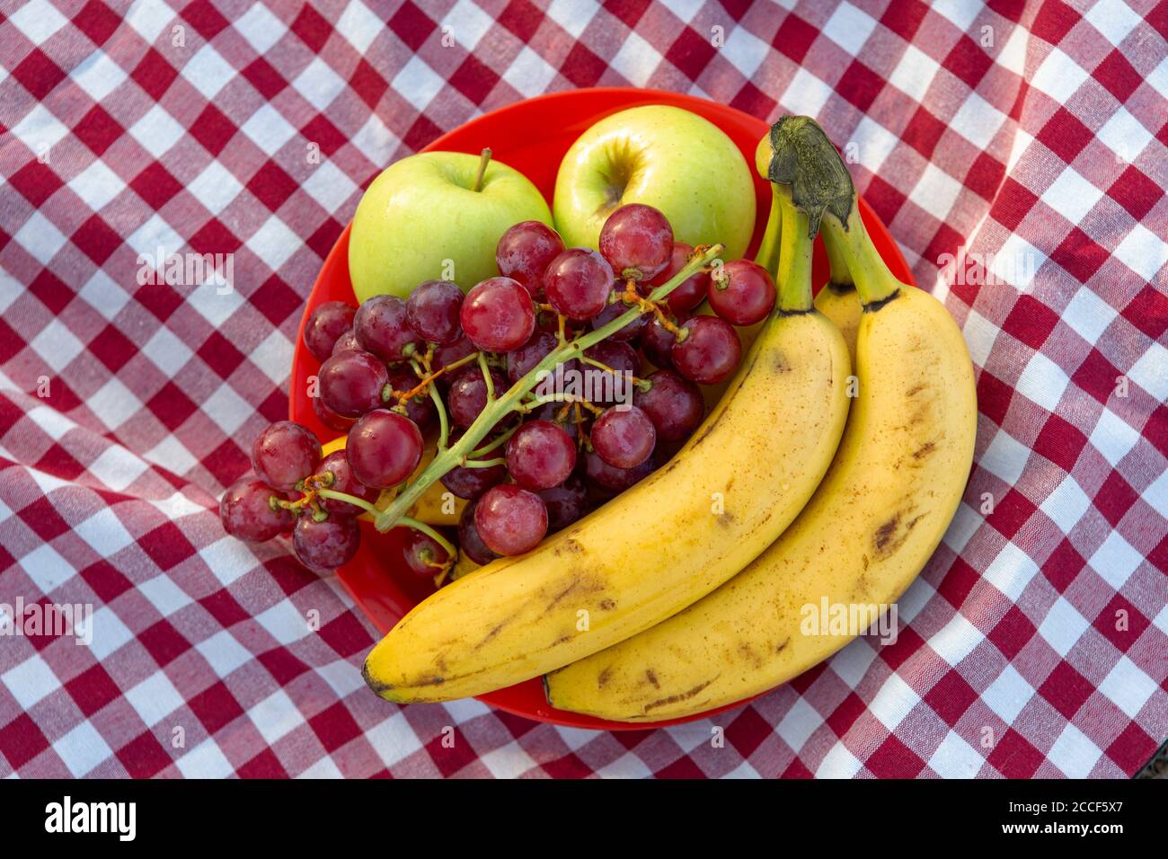 Plato reutilizable con fruta, plátano, manzana, uvas colocadas en un típico  mantel de camping de cuadros rojos y blancos Fotografía de stock - Alamy