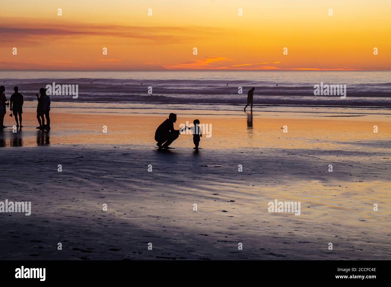 Puesta de sol a última hora de la noche, la Jolla Beach, papá y niño pequeño en silueta, papá y niño que se acerca el uno al otro Foto de stock