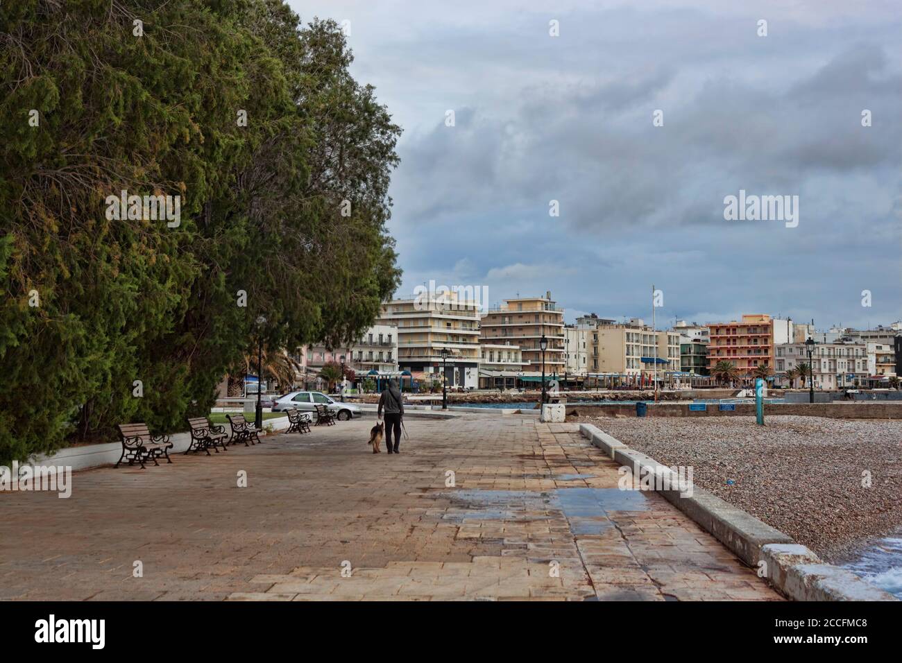 LOUTRAKI, GRECIA - 27 DE JUNIO de 2020: En un día nublado en el desierto paseo marítimo de Loutraki, sólo un hombre con un perro Foto de stock