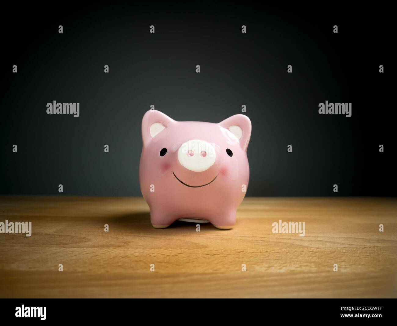 Piggy Bank, Ahorro, Moneda concepto : Banco piggy rosa con cara de sonrisa en mesa de madera con fondo negro Foto de stock