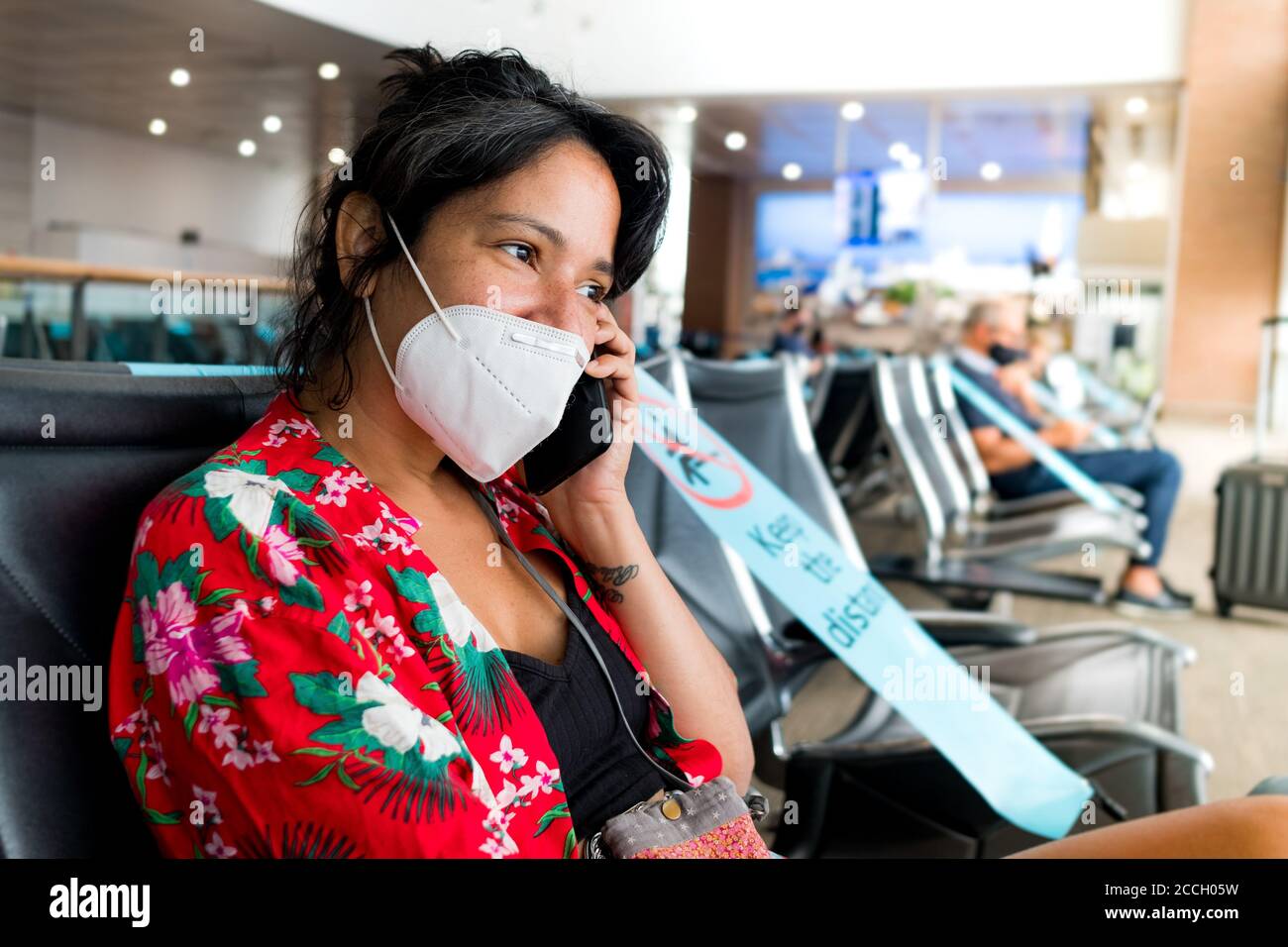 Barcelona, España - 20 de agosto de 2020: Una joven se sienta dentro del aeropuerto con máscara, hablando por teléfono, durante un pande global coronavirus Foto de stock