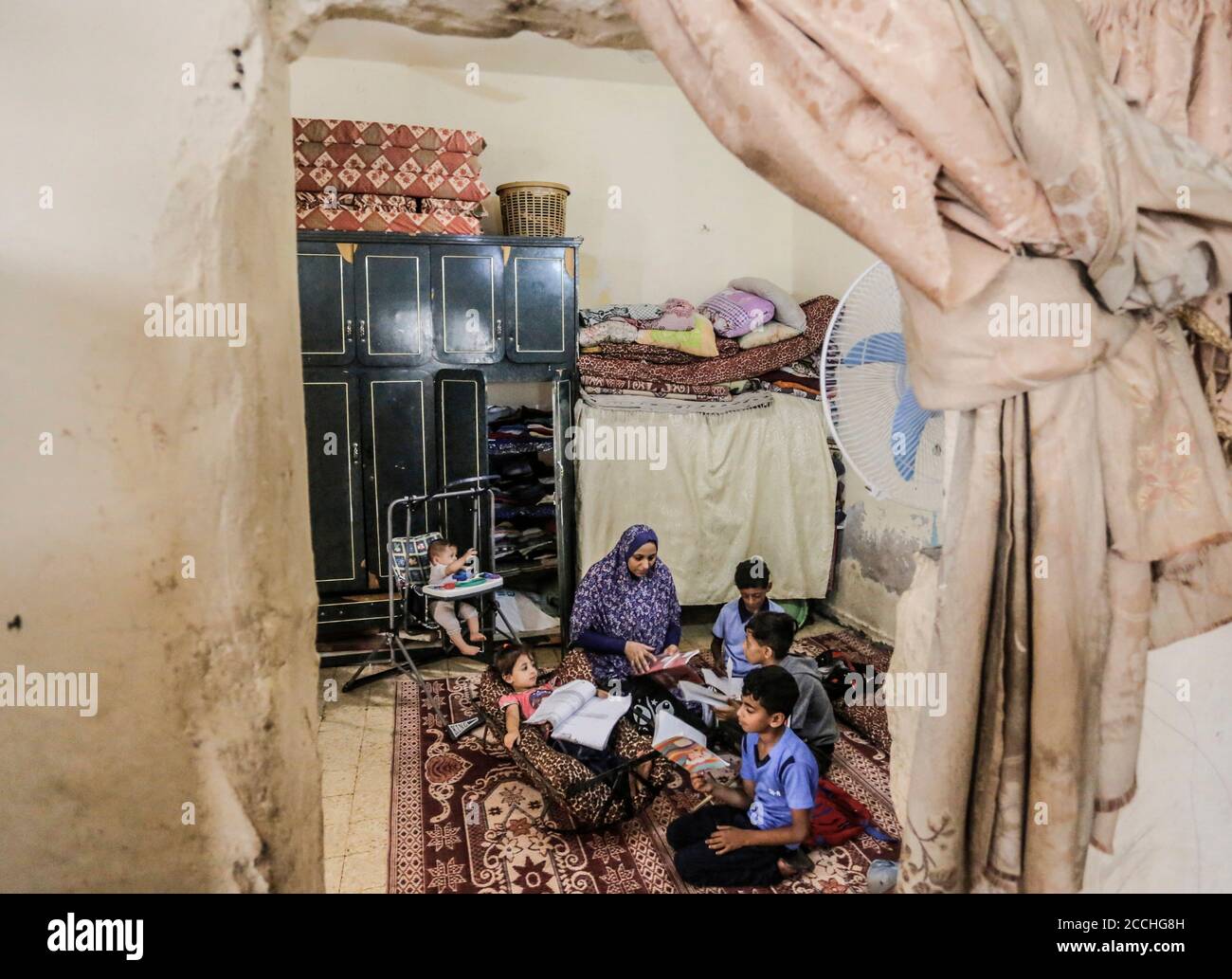22 de agosto de 2020, Ciudad de Gaza, la Franja de Gaza, Palestina: La familia del palestino Abu Mazen Dahir se sienta en su casa en el barrio Shejaiya en la Franja de Gaza oriental. Una familia palestina de la Franja de Gaza tiene más de 84 miembros que viven en una casa vieja y deteriorada que consta de sólo 3 plantas, Y toda una familia formada por un padre, madre y 4 hijos murieron en ella hace años debido a un incendio que estalló en su habitación, recibieron numerosas promesas de los funcionarios para restaurar la casa en ruinas, sin éxito hasta este momento. (Imagen de crédito: © Mahmoud Issa/Quds Net News Foto de stock