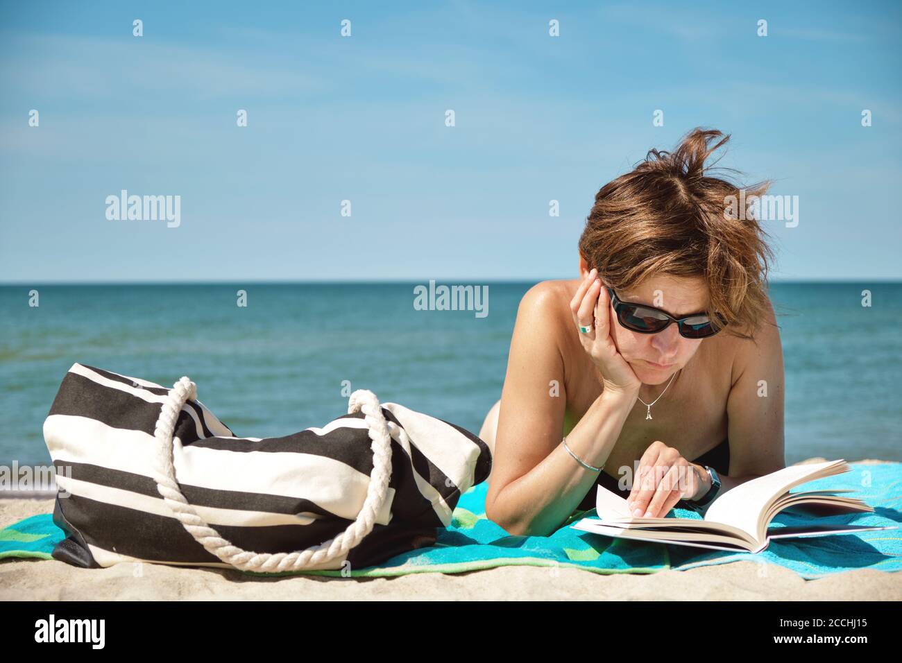 Primer plano sobre la mujer caucásica de mediana edad en bikini tomar el sol la playa y la lectura de un libro en el luminoso día de verano Foto de stock