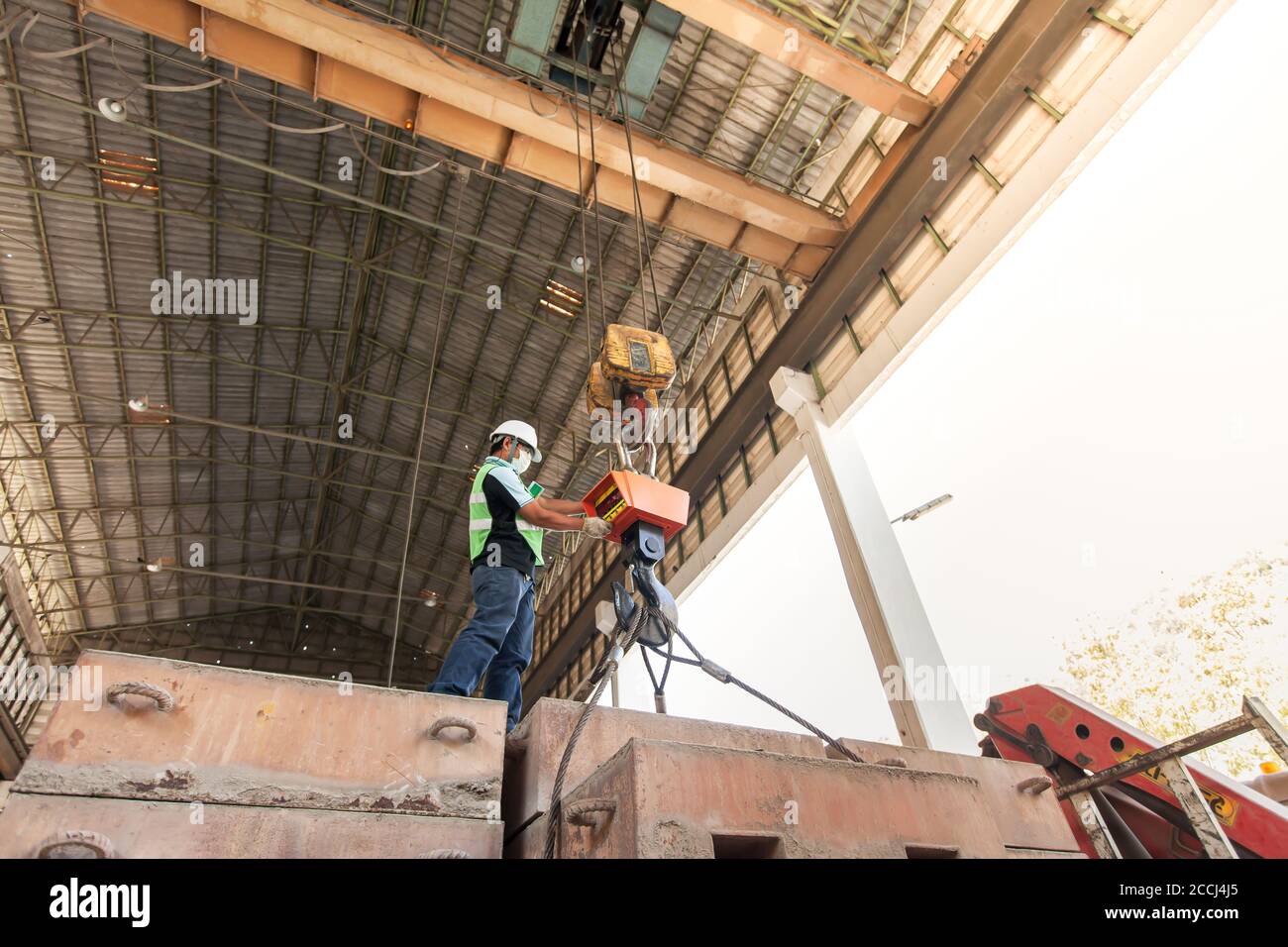 Un ingeniero asiático masculino con equipo de protección que controla el elevador de cable eléctrico, elevador de hierro pesado gancho de elevación de la plataforma de la estructura. Foto de stock