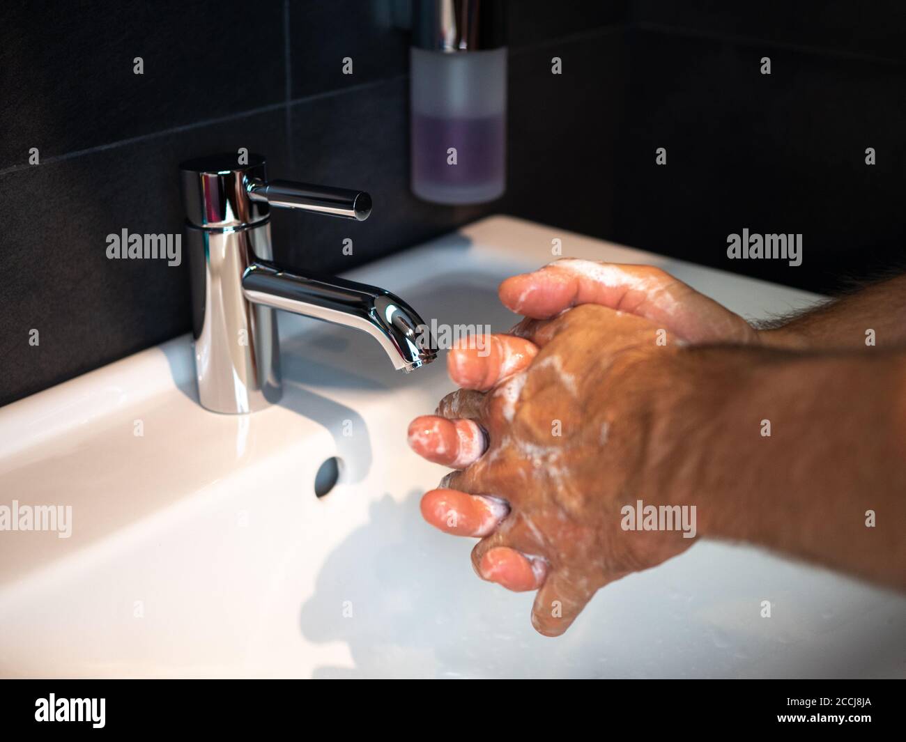 Lavarse las manos higiene personal hombre lavarse las manos frotar el jabón durante 20 segundos siguiendo los pasos, limpiar las muñecas y enjuagarse bajo el agua en el baño de la casa. Foto de stock
