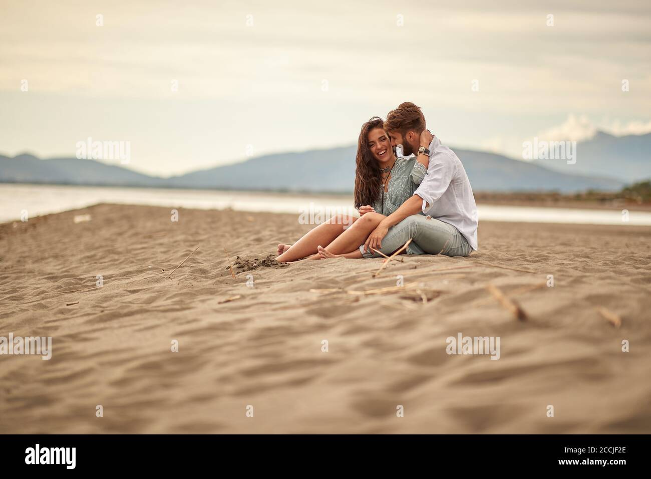 Pareja joven enamorada sentada en un abrazo en el playa en un tiempo hermoso Foto de stock