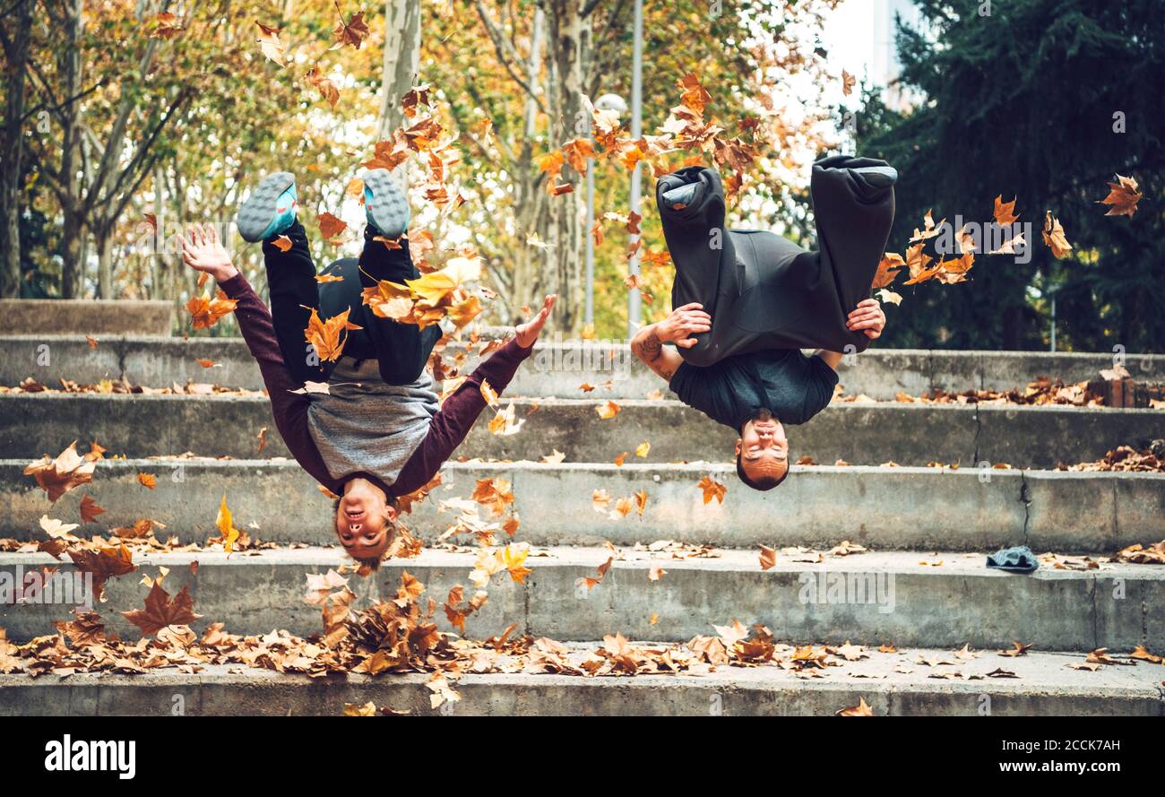 Amigos masculinos saltando contra la escalera en el parque público durante el otoño Foto de stock