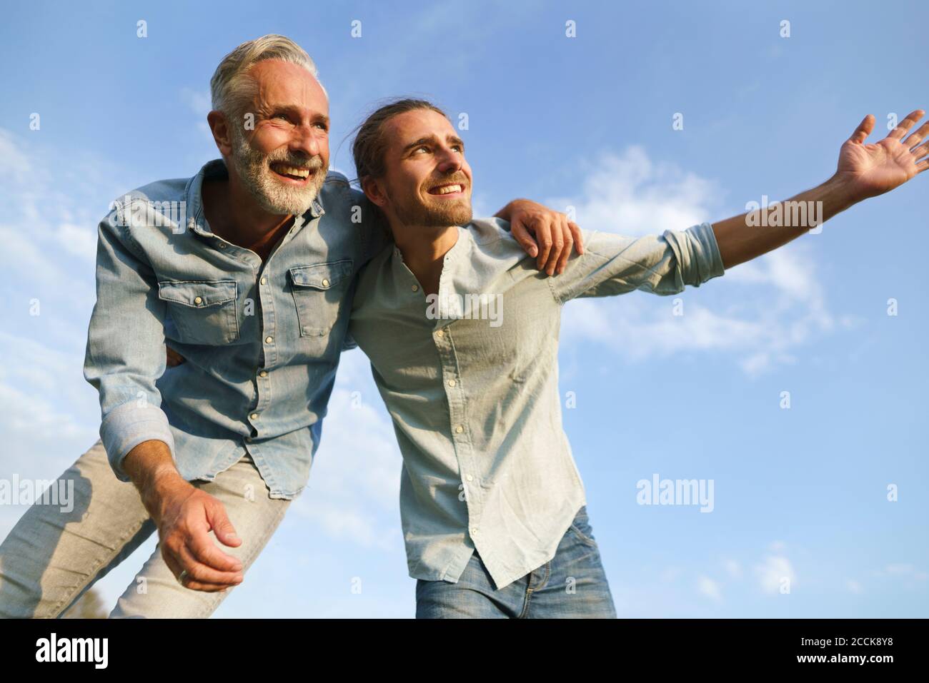 Padre despreocupado con hijo adulto bajo el cielo azul Foto de stock