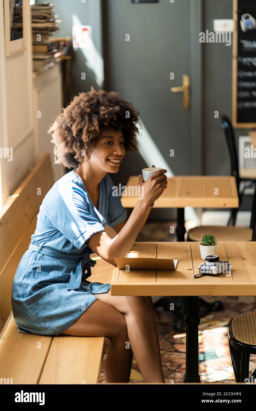 Una mujer pensativa sosteniendo una taza de café mientras se sentaba en la mesa café Foto de stock