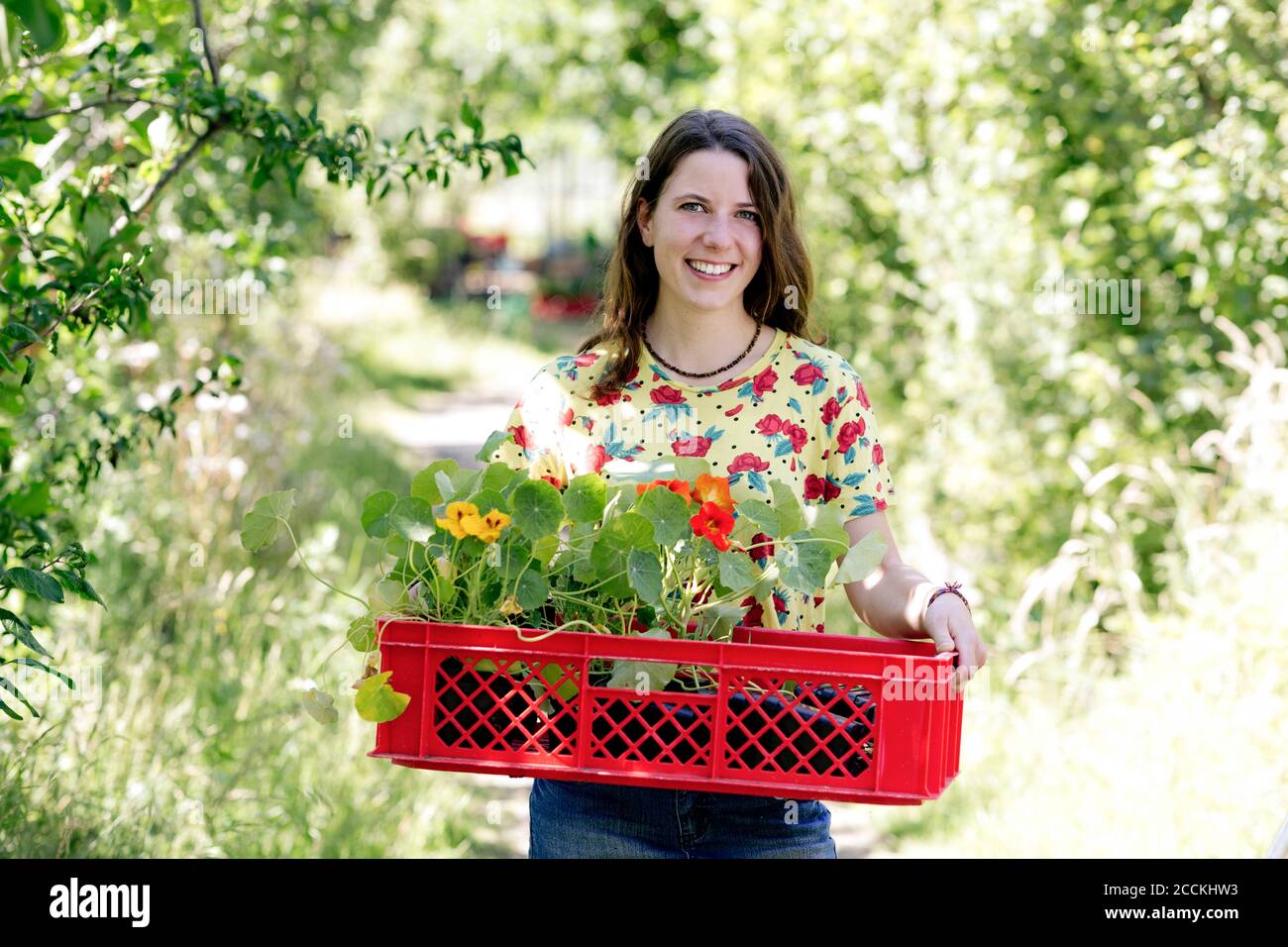 Mujer joven sonriente que lleva nasturtium en la cesta en la granja Foto de stock