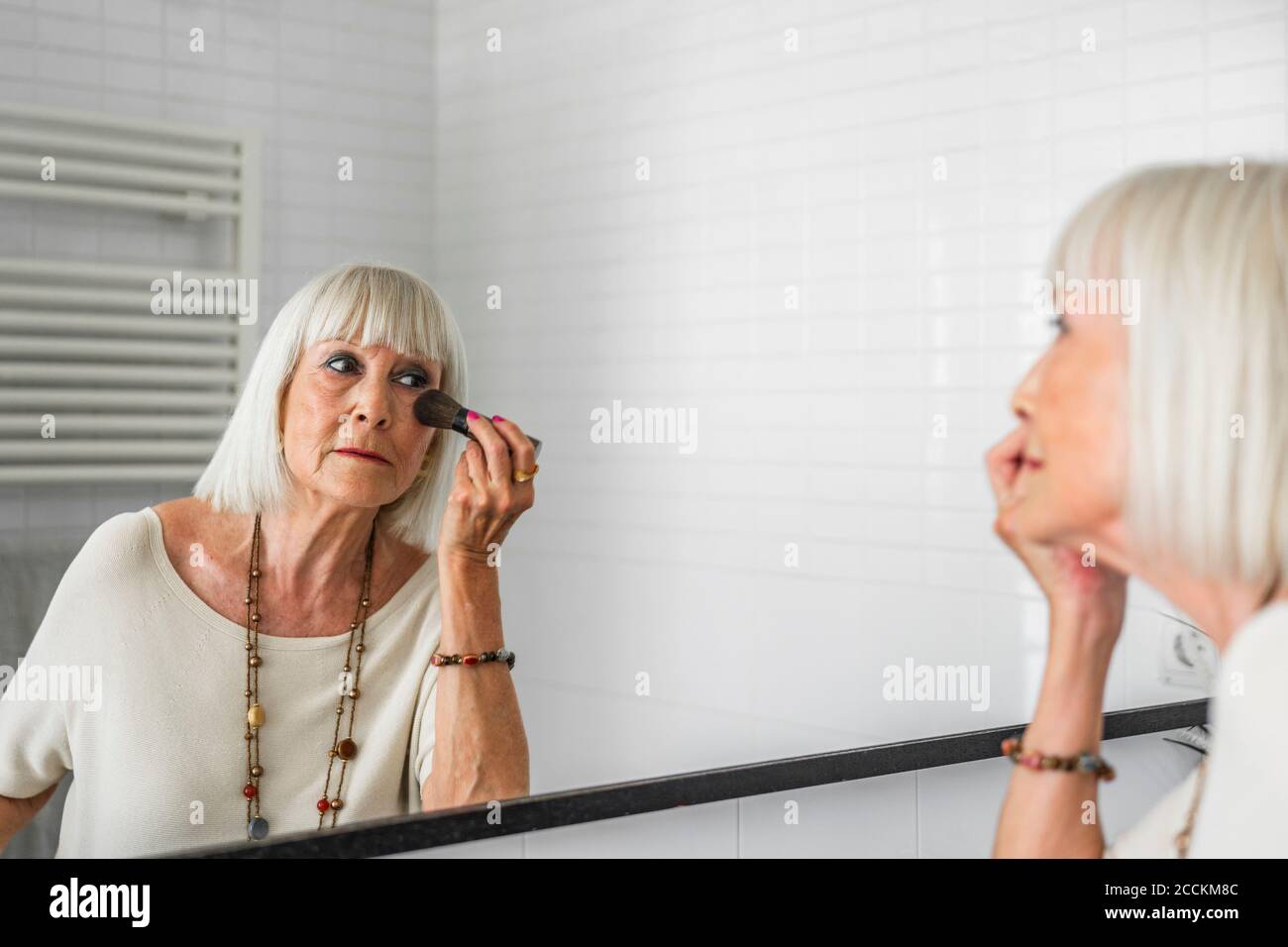 Elegante mujer mayor aplicando maquillaje mientras mira en el espejo inicio Foto de stock