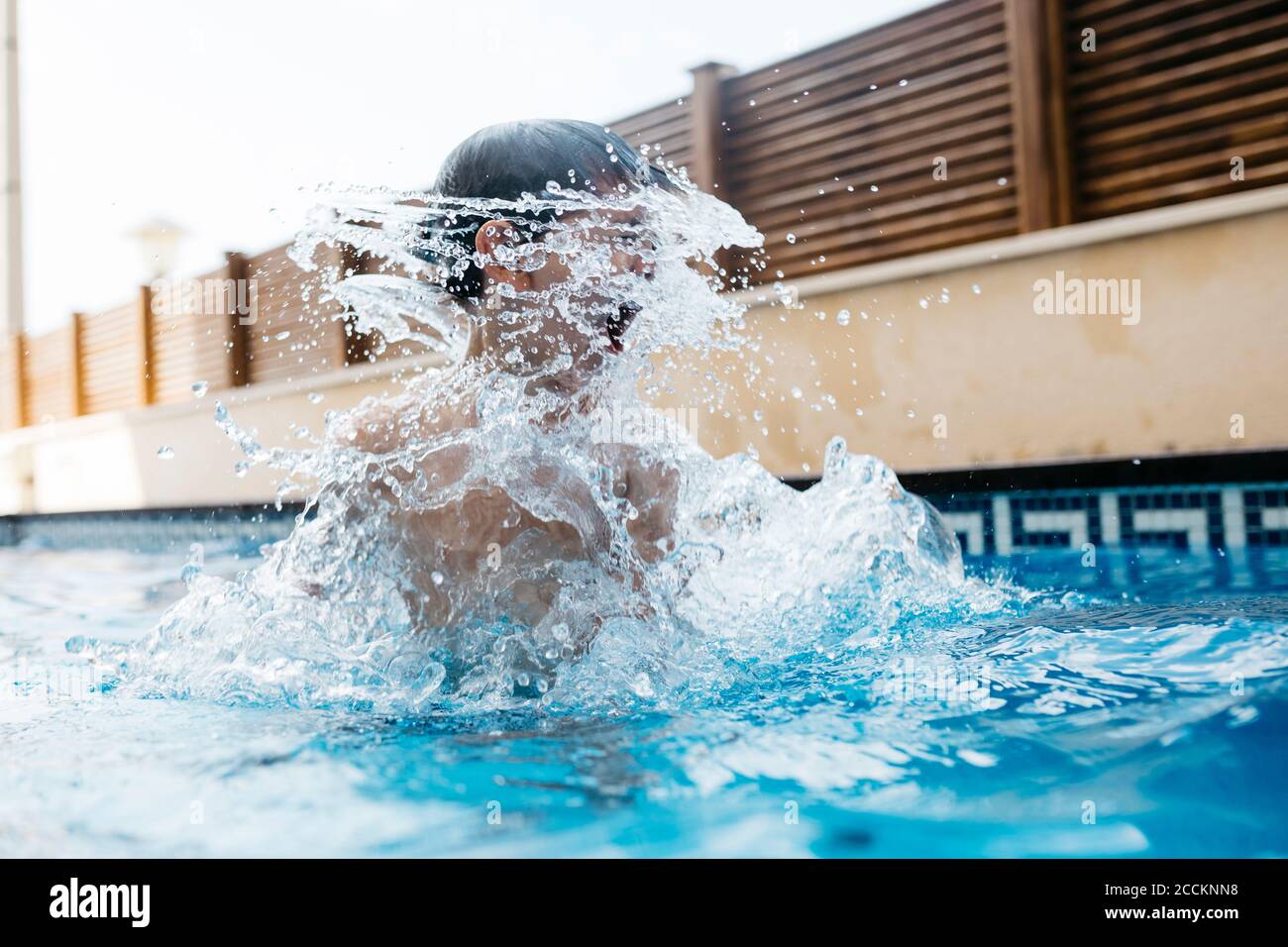 Niño chapoteando agua en la piscina durante el verano Foto de stock