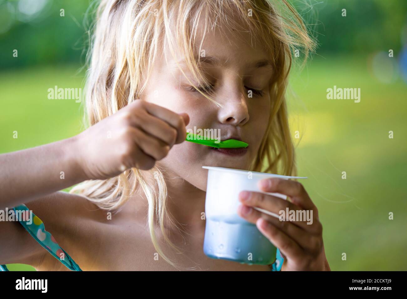 Chica rubia comiendo helado en una taza desechable Foto de stock