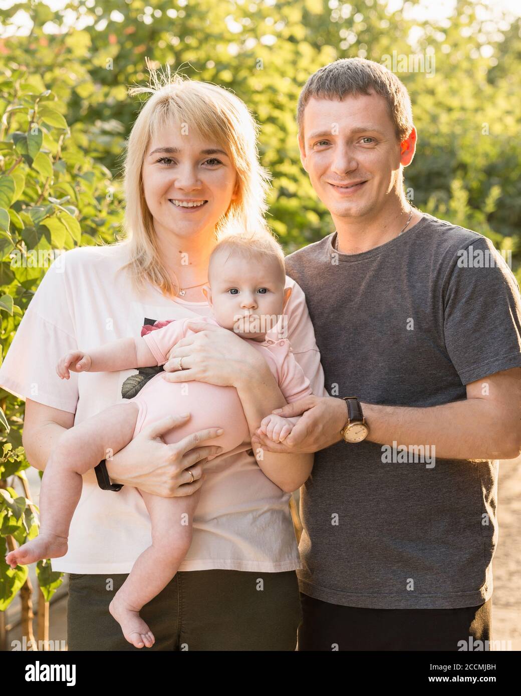Una Familia Joven Con Un Nino Pequeno Caminando En El Verano En La Calle Sonrien Y Miran Al Marco Papa Mama Y Bebe En Un Soleado Dia De Verano Fotografia De Stock