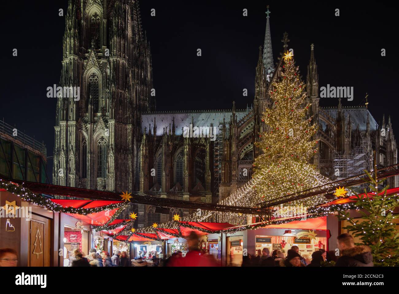 Paisaje nocturno, Weihnachtsmarkt, mercado de Navidad en Colonia, con varios puestos iluminados decorados frente al árbol de Navidad y la Catedral de Colonia. Foto de stock