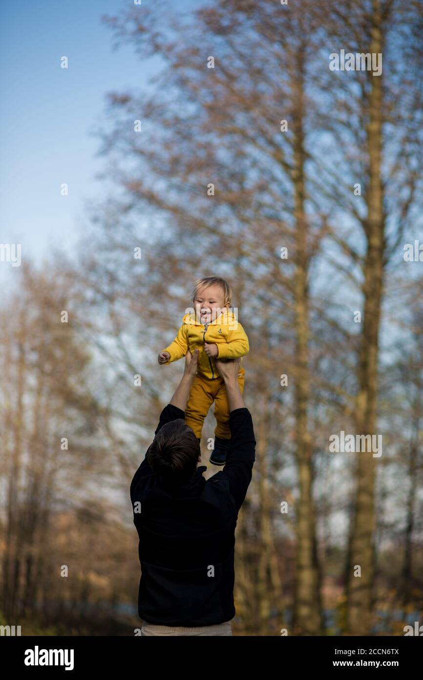 Papá lanza a un bebé en una chaqueta amarilla al aire, el niño se ríe y se  divierte Fotografía de stock - Alamy