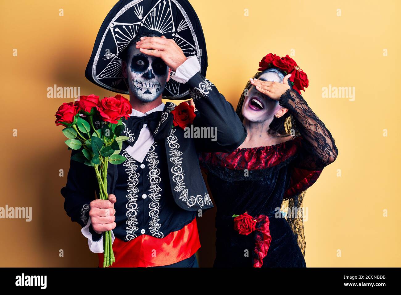 Pareja joven con el día mexicano de la muerte traje de rosas tensionadas y frustradas con la mano en la cabeza, cara sorprendida y enojada Foto de stock