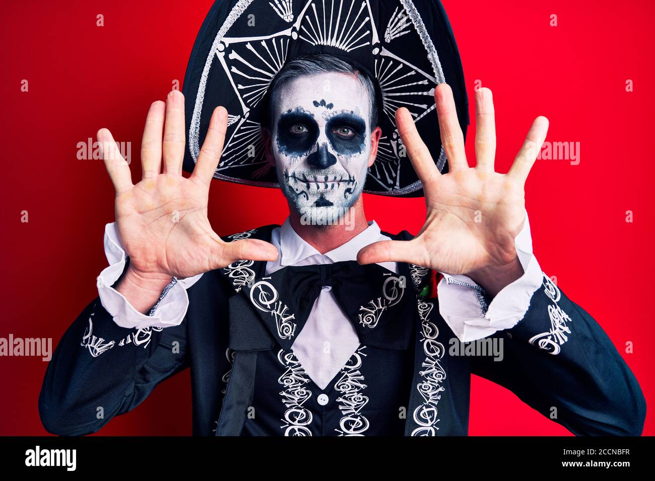 Hombre joven con traje mexicano de día muerto sobre rojo mostrando y señalando con los dedos número diez mientras sonriendo confidente y feliz. Foto de stock