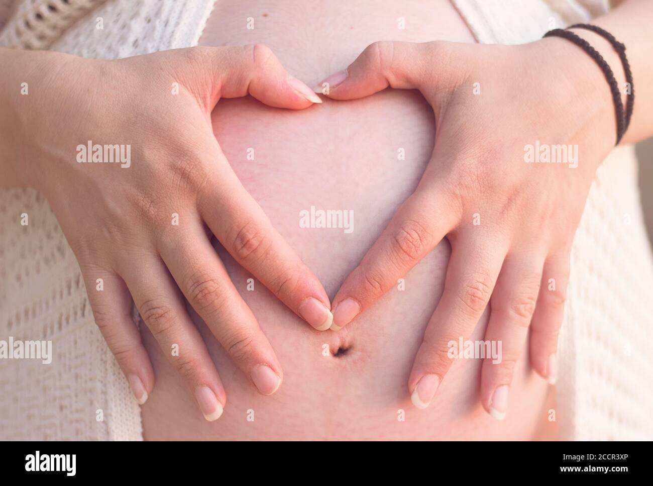 Mujer embarazada sosteniendo sus manos en forma de corazón en su vientre. Símbolo del corazón, concepto de maternidad y familia Foto de stock