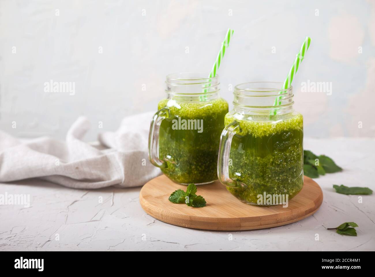 Dos tarros con batidos verdes sobre un soporte de madera sobre un fondo gris concreto. Desintoxicación. Copiar espas. Foto de stock