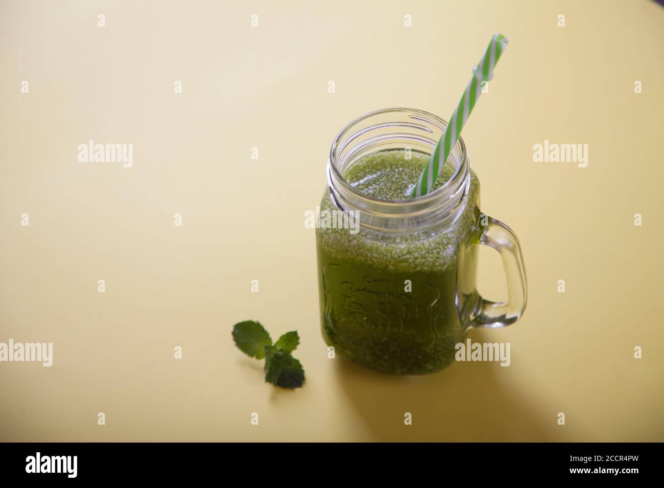 Batido de hierbas frescas y verdes en un tarro con una paja sobre un fondo amarillo. Vista superior. Copiar espas Foto de stock