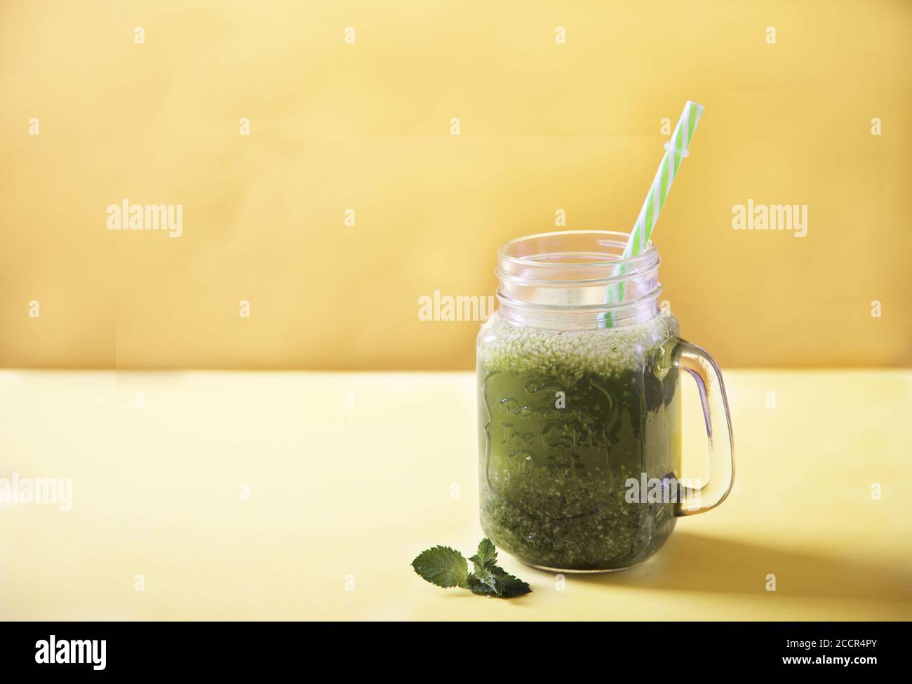 Batido verde fresco en un tarro de taza y una hoja de menta sobre un fondo amarillo. Copiar espas Foto de stock