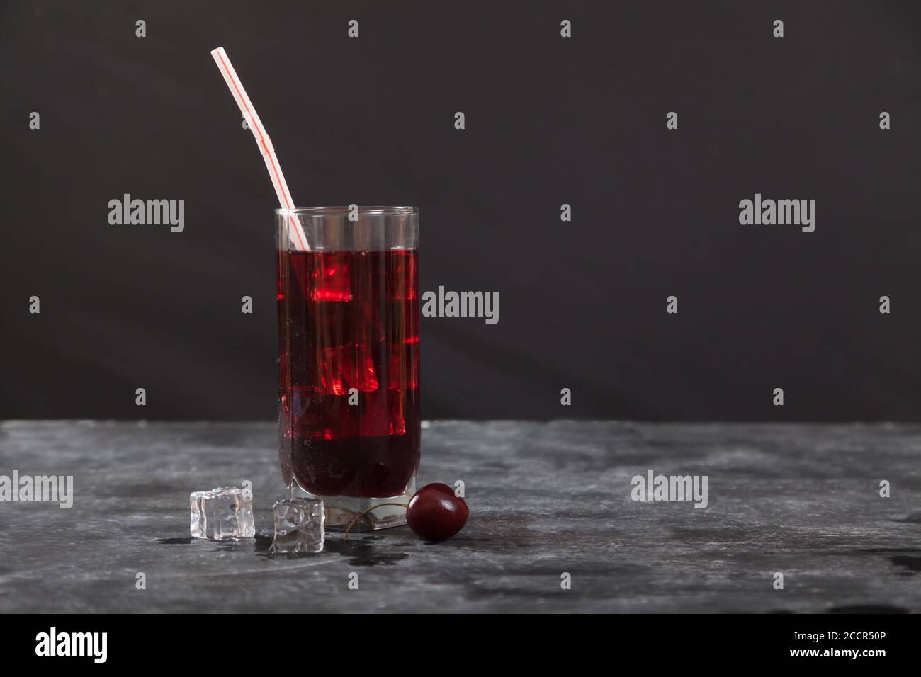 Jugo de cereza frío con hielo en un vaso con una paja se apoya sobre un fondo negro. Copiar espas Foto de stock