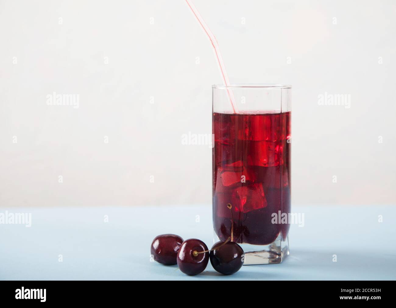 Un vaso de jugo de cereza con hielo y cerezas en una mesa blanca. Copiar espas Foto de stock