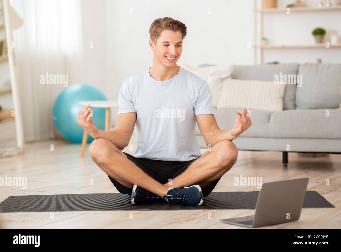 El hombre riendo sentado en el loto pose y tratando de meditar sobre la alfombra Foto de stock