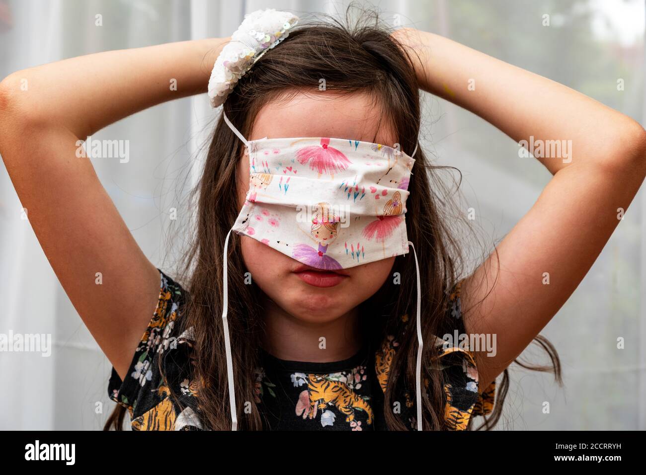 Niña que intenta en la cubierta casera de la cara durante el Covid-19 pandemia Foto de stock