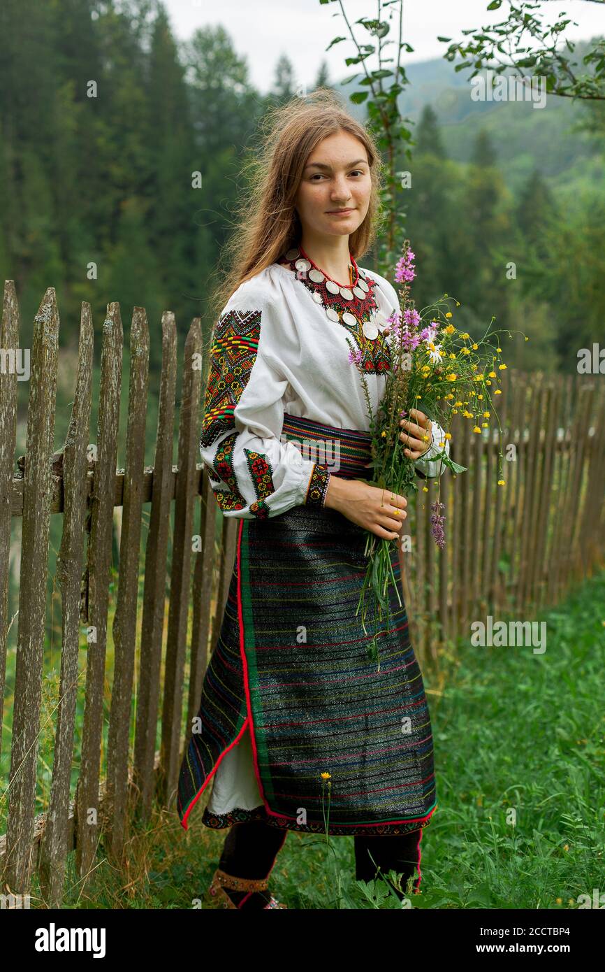 chica con pelo suelto con un ramo de flores silvestres se pone de pie en una valla de madera Foto de stock