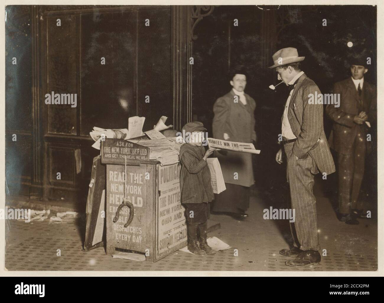 Jerald Schaitberger de 416 W. 57th St. N.Y. que ayuda a un niño mayor a vender papeles hasta las 10 P.M. en Columbus Circle. 7 años. 9-30 P.M., 8 de octubre de 1910. Foto de stock