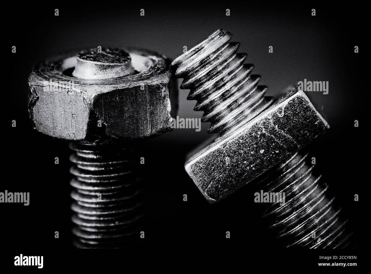 Una imagen monocroma de arte fino de dos tornillos mecanizados que se inclinan junto con tuercas hexagonales y cuadradas. Foto de stock