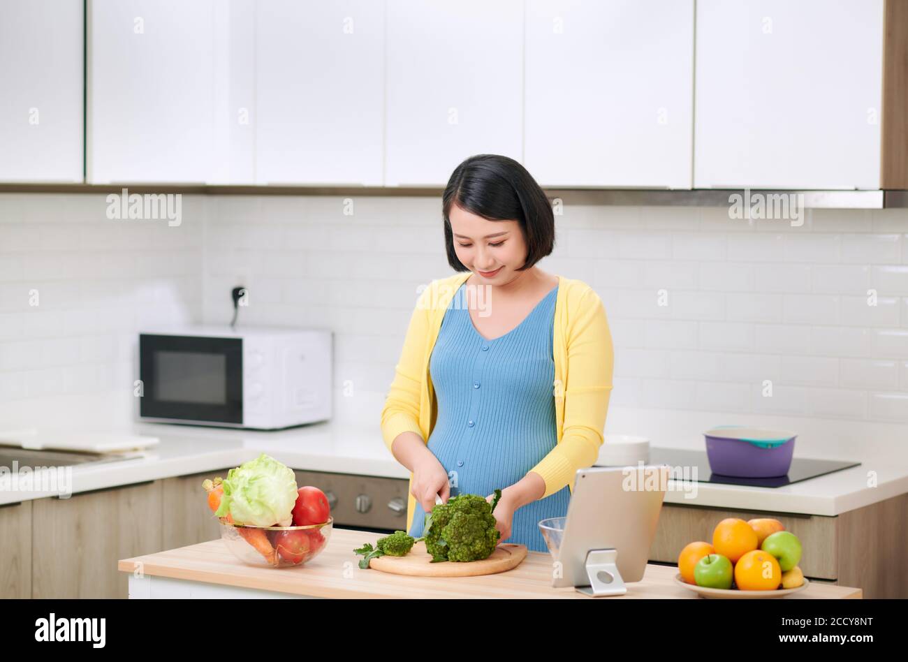 Mujer embarazada cortando brócoli para ensalada verde fresca, la mujer prepara una deliciosa cena orgánica en casa Foto de stock