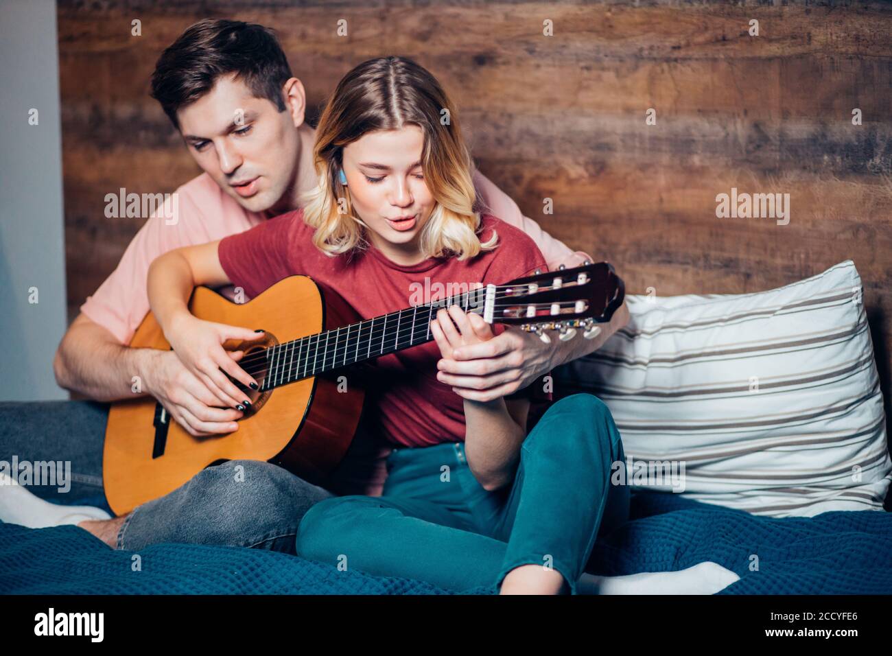https://c8.alamy.com/compes/2ccyfe6/una-pareja-caucasica-encantadora-toca-la-guitarra-sentado-en-la-cama-un-joven-ensenando-a-su-novia-a-tocar-la-guitarra-2ccyfe6.jpg