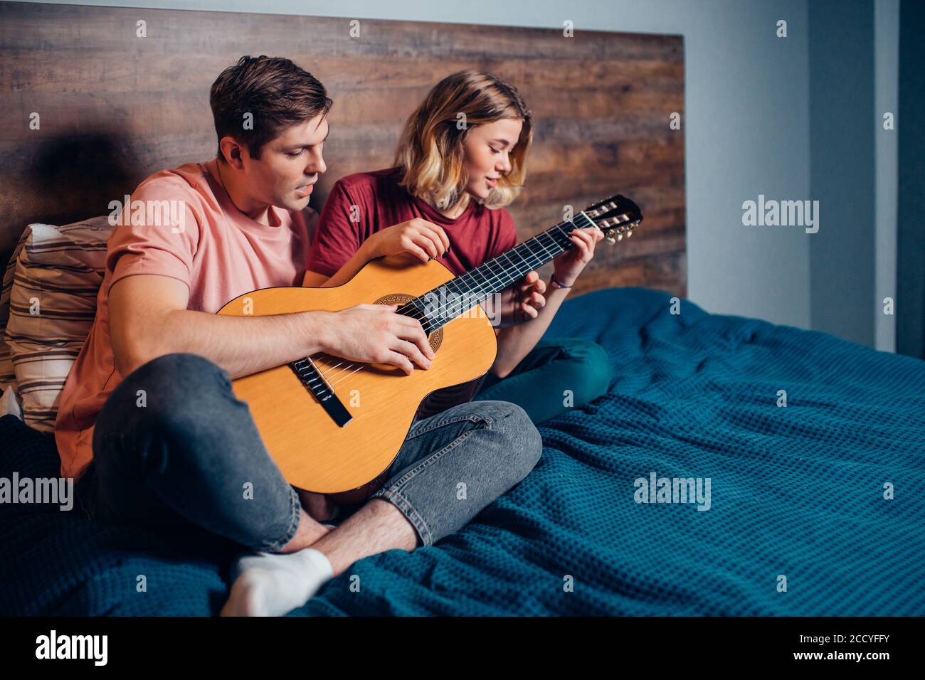 pareja encantadora, gente joven tocando la guitarra en casa sentada en la  cama Fotografía de stock - Alamy