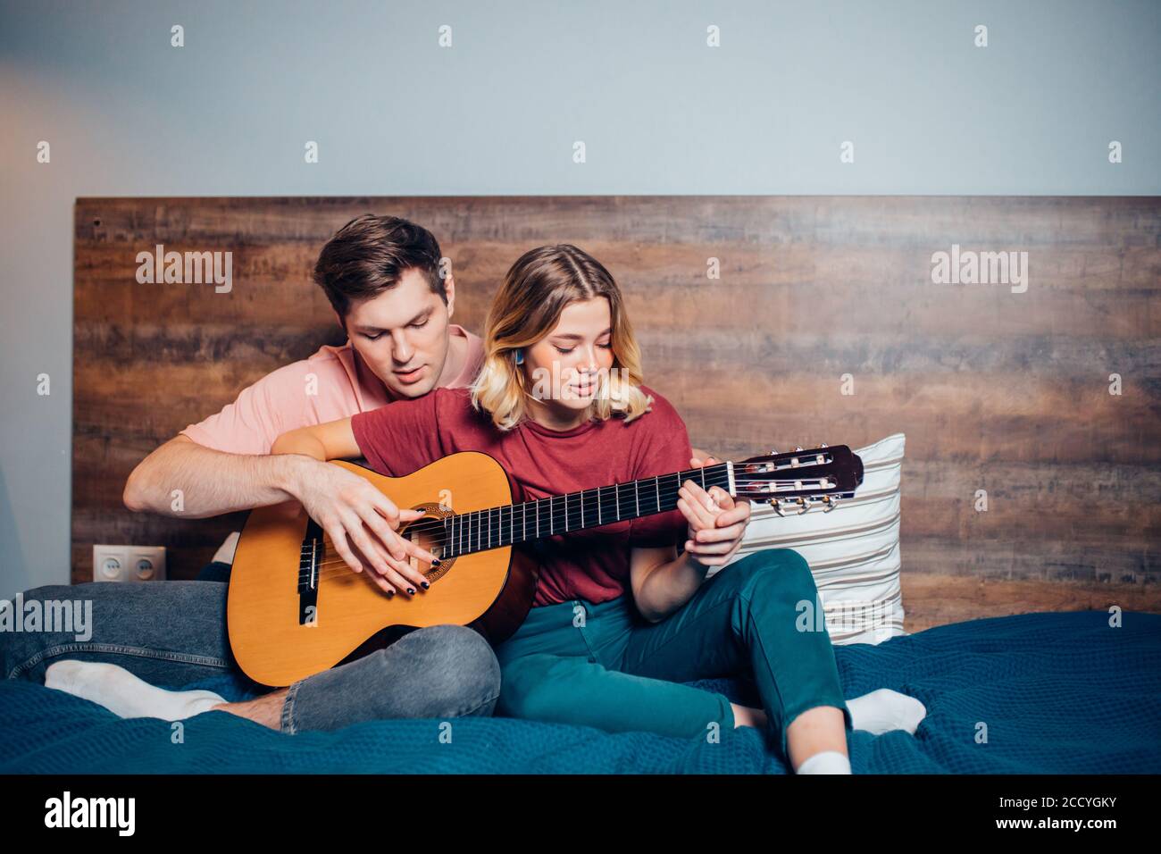 https://c8.alamy.com/compes/2ccygky/joven-novio-ensenando-a-su-novia-a-tocar-la-guitarra-en-casa-pareja-encantadora-usando-ropa-informal-en-el-dormitorio-juntos-2ccygky.jpg