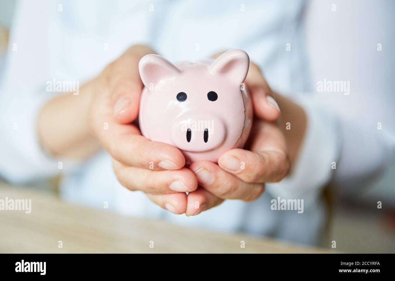 Las manos sostienen un banco de pigmeo rosa como símbolo de ahorro e inversión Foto de stock